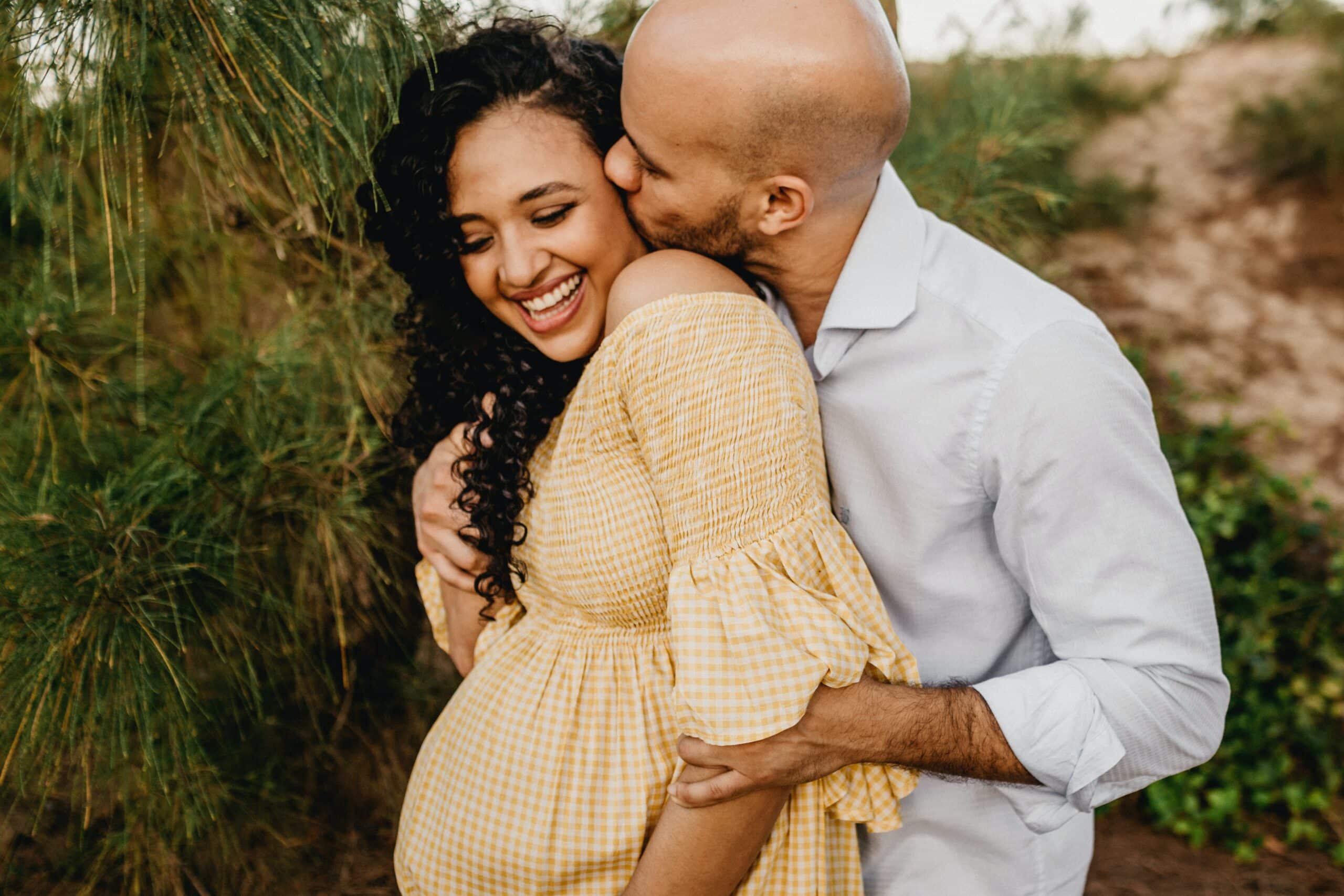 man hugging pregnant woman and kissing her cheek from behind